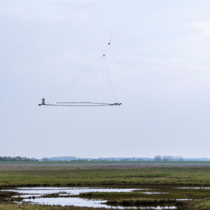 Gathering knowledge to address climate change: TOPSOIL's airborne, cutting-edge technology tracks and predicts climate impacts by mapping the soil structures deep beneath our feet. Photo: Nick Wenmaekers An airborne device is flown over a landscape by a helicopter.