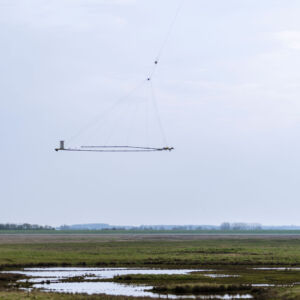Gathering knowledge to address climate change: TOPSOIL's airborne, cutting-edge technology tracks and predicts climate impacts by mapping the soil structures deep beneath our feet. Photo: Nick Wenmaekers An airborne device is flown over a landscape by a helicopter.