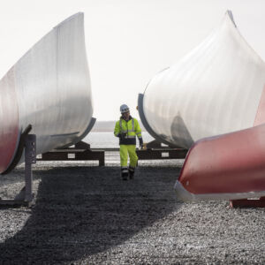 Inn2POWER: Based on 2018 figures, the offshore wind industry and its supply chains account for 200,000 jobs in the North Sea Region alone. However, the demand for qualified personnel in the offshore wind industry remains high. This photo symbolises the importance of trained staff in an expanding industry. In addition to engineering and technology skills, management capacity needs to increase as well. Therefore, Inn2POWER developed the first MBA programme specifically for the offshore wind industry. A worker walking in between wind turbine blades stored on the ground.