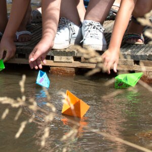 CATCH: Enschede, the Netherlands - a public space serving in water collection, as playground, and for public awareness raising. In a playful way, children learn about water's multiple functions and about climate impacts. CATCH accelerates the redesign of urban water management of midsize cities in the North Sea Region, helping them become climate resilient, liveable and profitable in the long term. Paper boats being put into water by children's hands.