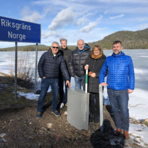 Cooperation across the Sweden-Norway border in the CORA pilot "Cross-border fibre - taking broadband from Sweden to Norway". The photo shows the CORA project partners and stakeholders at the fibre cabinet on the border between Sweden and Norway. From this cabinet, the fibre can be extended from the Swedish to the Norwegian side. A group of people standing in front of a mountainous landscape and a signpost marking the border between Norway and Sweden.