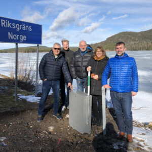Cooperation across the Sweden-Norway border in the CORA pilot "Cross-border fibre - taking broadband from Sweden to Norway". The photo shows the CORA project partners and stakeholders at the fibre cabinet on the border between Sweden and Norway. From this cabinet, the fibre can be extended from the Swedish to the Norwegian side. A group of people standing in front of a mountainous landscape and a signpost marking the border between Norway and Sweden.
