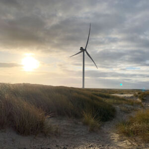 DUAL Ports: At the coast by the Danish port o4f Hvide Sande, three wind turbines produce sustainable energy for local district heating providing heat for the citizens. Dunes and a large wind turbine at dusk in Hvide Sande, Denmark.