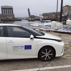 HyTrEc2: A Fuel Cell car in the foreground and the Energy Observer in the background. The Energy Observer is the first hydrogen powered vessel which is entirely energy self-sufficient. The Energy Observer has heard of the amazing work HyTrEc2 are doing and requested a visit. The photo shows the companionship that exists between those blazing the trail in hydrogen transport. Each project seeks to promote new technologies and help the world to transition away from damaging fossil fuels. Photo: Aberdeenshire (HyTrEc2 partner). White hydrogen-fueled car used in the North Sea Region funded HyTrEc2 project.