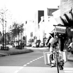 SURFLOGH: Powerful contrast (black and white) and physically powerful (heroic). Clearing our streets from C02. Business initiatives/start up pilots supported by SURFLOGH. Cyclist delivering goods in city.