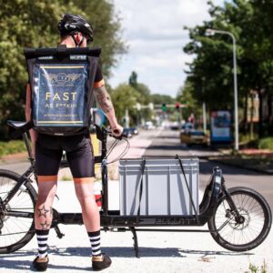 SURFLOGH: Cargobike as alternative delivery mode. Business initiative/start-up pilots supported by SURFLOGH. Young man with his cargobike standing on road.