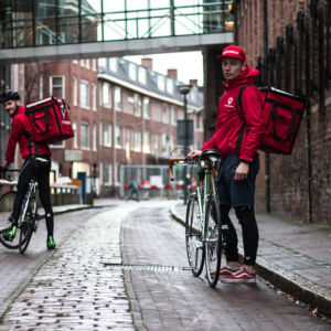 SURLOGH: Heroes of our time…cargo bike delivery is a booming business during lockdown. All these are business initiatives/start up pilots supported by SURFLOGH. Two cargo bike riders standing in a street in red jackets holding their bikes.