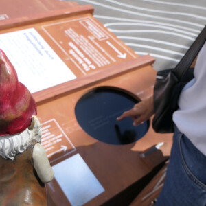 North Sea Wrecks: Communication concept for children: Gulliver, the garden gnome, tells children the story of the North Sea Wrecks project. Here he explores the multimedia stations of the exhibition. Photo: Cornelia Riml A person putting his finger on a window in a wooden box.