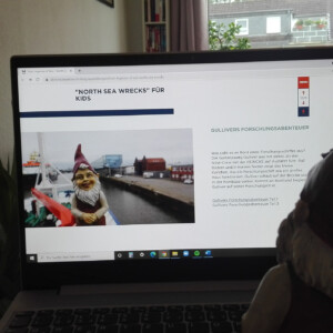 North Sea Wrecks: concept for children: Gulliver, the garden gnome, tells children the story of the North Sea Wrecks project (NSW) and the EU support. Photo: Cornelia Riml Garden gnome looking at laptop screen featuring himself in front of a harbour.